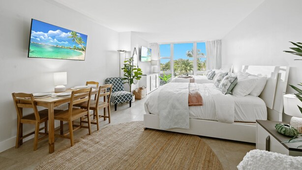 Quarto moderno com uma cama grande, uma mesa de jantar com cadeiras e uma TV na parede.