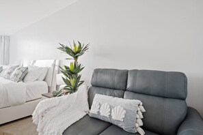 A modern bedroom with a grey sofa, a white bed with patterned pillows, and a potted plant. - Ocean Manor 1BR - Beachfront, Pool & Tiki Bar (Fort Lauderdale)