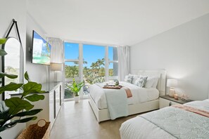 Een moderne slaapkamer met een groot bed, een televisie en een balkon met uitzicht op palmbomen.