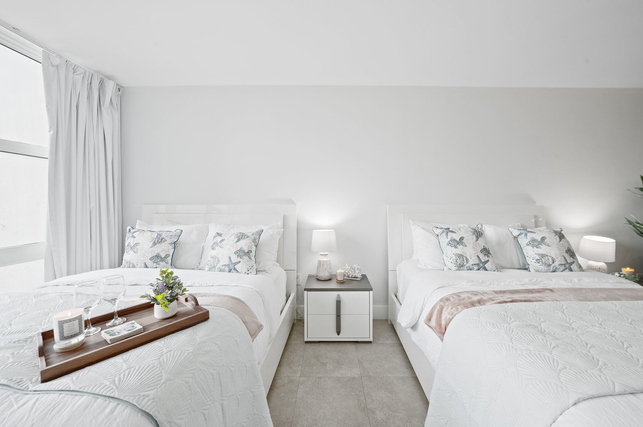 A modern bedroom with two beds, a nightstand, a tray with candles, and a potted plant.