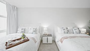 A modern bedroom with two beds, a nightstand, a tray with candles, and a potted plant.