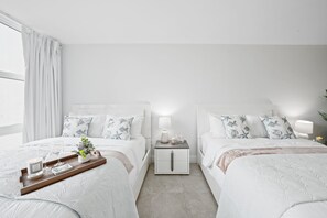 A modern bedroom with two beds, a nightstand, a tray with candles, and a potted plant.