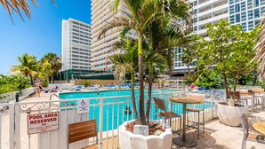 Uma área de piscina com aviso indicando que é exclusiva para hóspedes do hotel e proprietários de apartamentos. Há espreguiçadeiras e mesas ao redor da piscina, e palmeiras são visíveis.