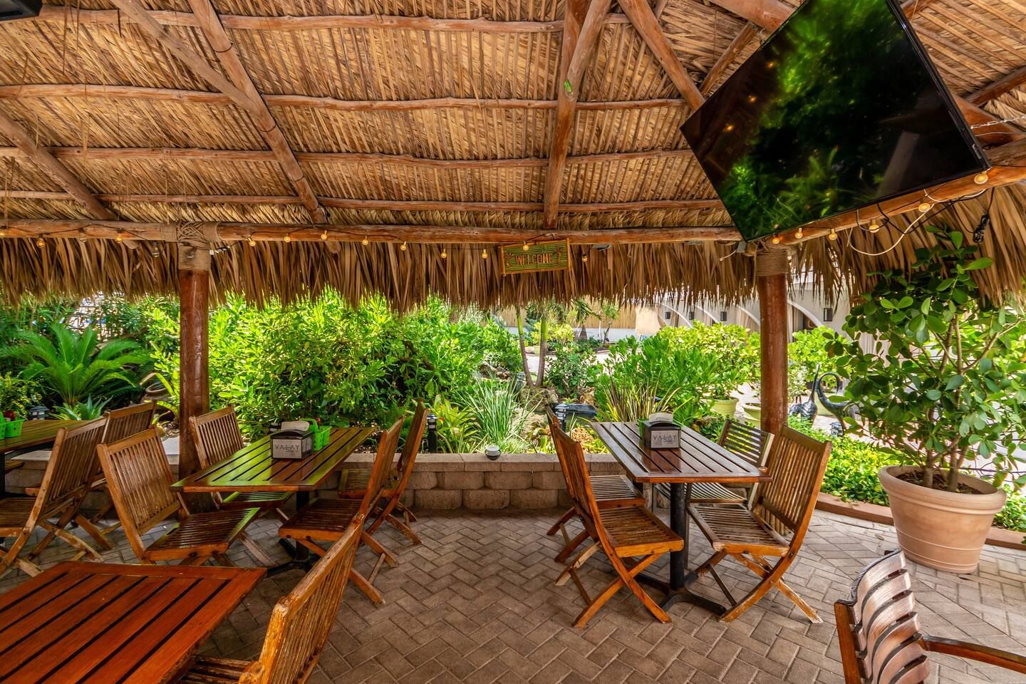 An outdoor patio with wooden furniture, a thatched roof, and potted plants.