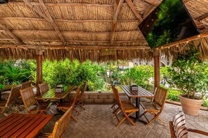 An outdoor patio with wooden furniture, a thatched roof, and potted plants.