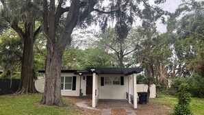 A small, single-story house with a covered porch, surrounded by large trees and a grassy yard. - PROMO NOW: City and Stadium Sanctuary Vibes (Orlando)