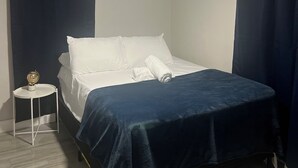 A neatly made bed with white linens, a dark blue bedspread, and a small bedside table with a globe. - PROMO NOW: City and Stadium Sanctuary Vibes (Orlando)