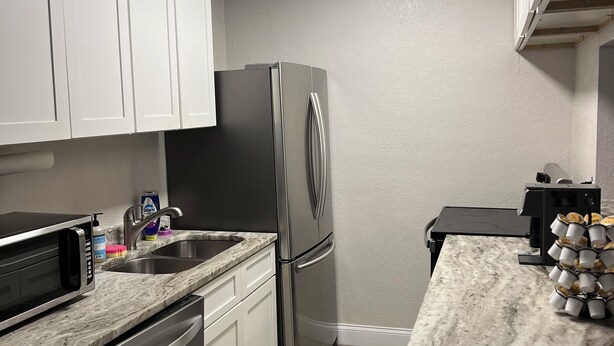 A compact kitchen with white cabinets, a stainless steel refrigerator, a microwave, and a coffee machine. - PROMO NOW: City and Stadium Sanctuary Vibes (Orlando)