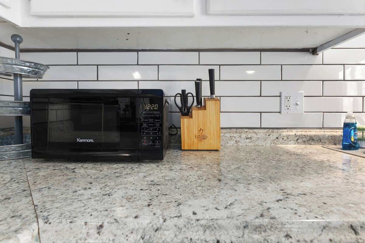 A kitchen with a black Kenmore microwave, a wooden utensil holder, and a blue cleaning product on the counter.