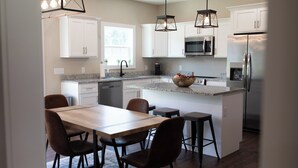 Une cuisine moderne avec des armoires blanches, un comptoir en granit, un réfrigérateur en acier inoxydable et un coin repas comprenant une table et des chaises en bois.