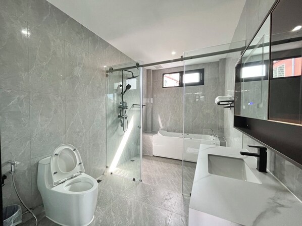 A modern bathroom with a glass-enclosed shower, a standalone toilet, a bathtub, and a large mirror.