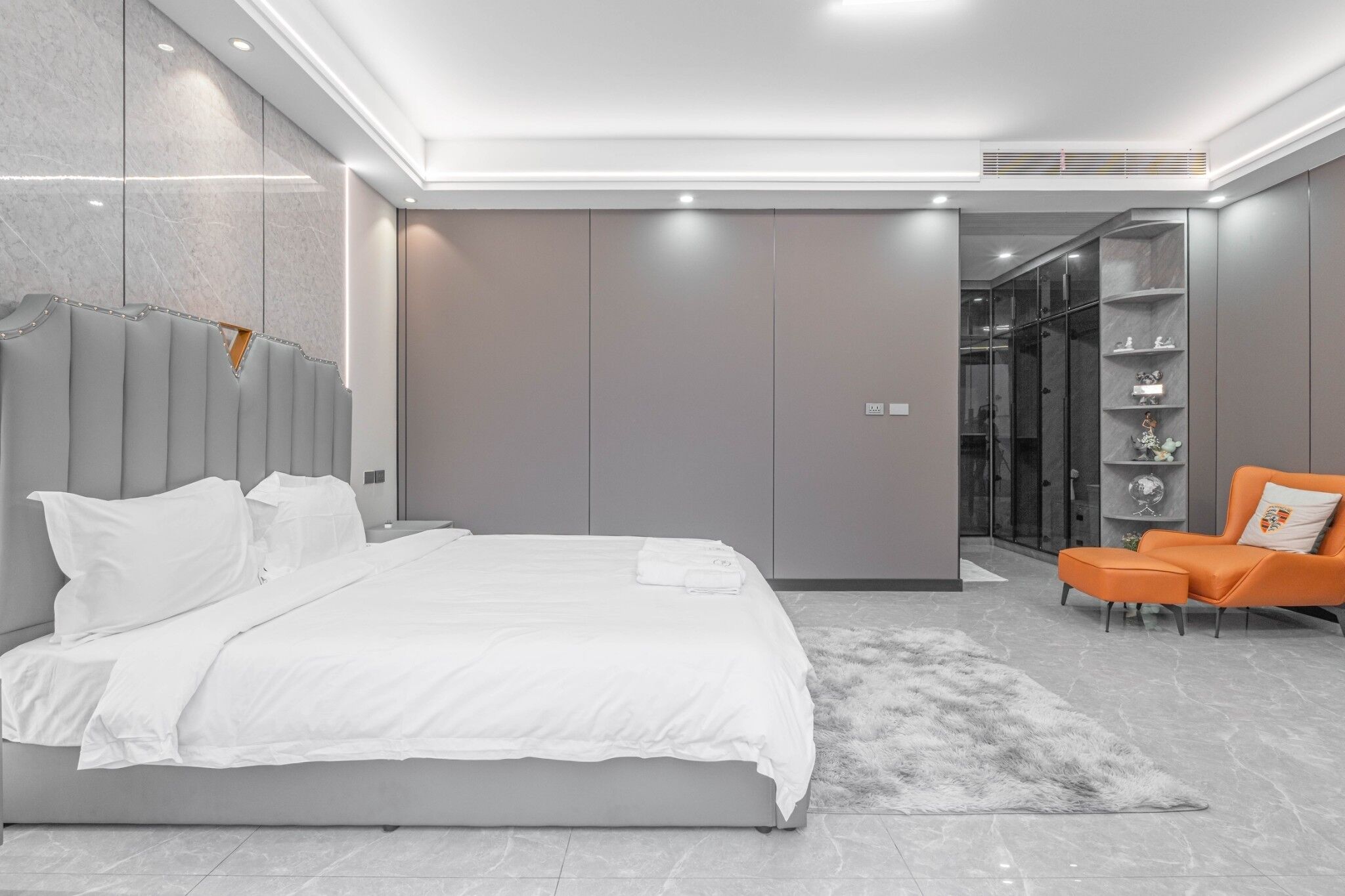 A modern bedroom with a large bed, grey walls, and a bright ceiling.