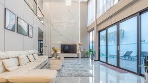 A spacious living area with a large sofa, a flat-screen TV, and a balcony with outdoor seating.