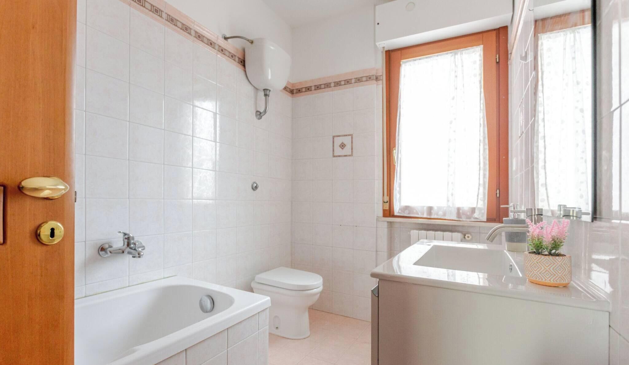 A bathroom with a bathtub, toilet, sink, and a window with curtains.
