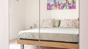 A bed with floral-patterned bedding, a cityscape painting above it, and a small potted plant on the nightstand. - Casa Pandolfi, Apartment With Internal Parking and AC (Pescara)