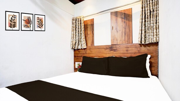 A bedroom with a wooden headboard, a bed with black and white bedding, and three framed leaf artworks on the wall.