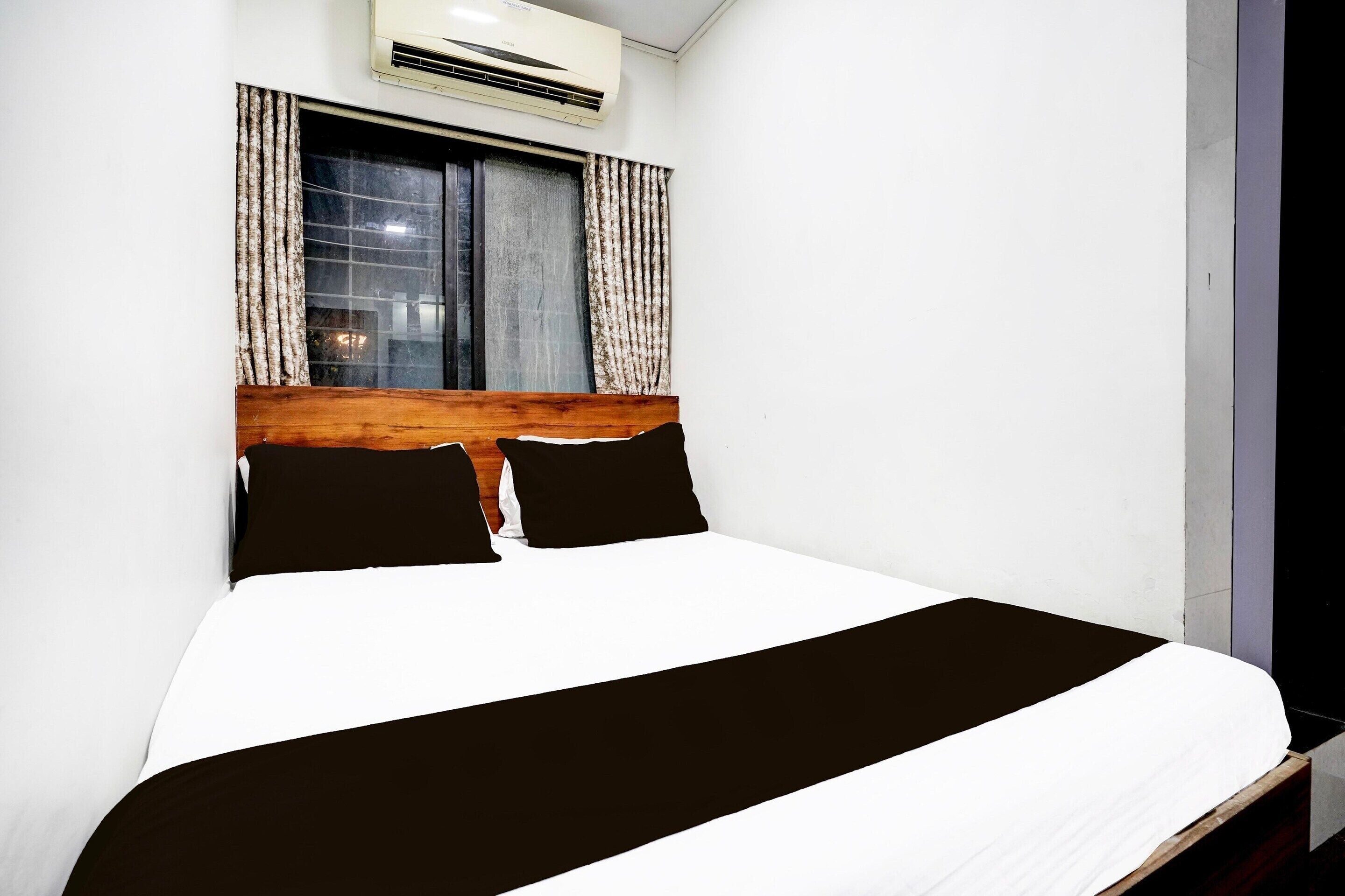 A hotel room with a bed, a wooden headboard, a window with curtains, and an air conditioning unit.