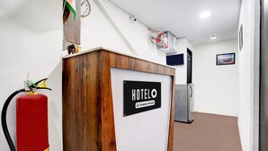A reception desk with a sign reading "HOTELO Company Serviced." A fire extinguisher is mounted on the wall to the left.
