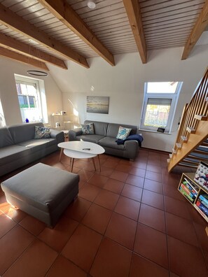 A living room with a sectional sofa, a coffee table, and a staircase. - Detached vacation home in Nessmersiel (near Deich) with private garden & wallbox (Dornum)
