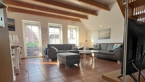 Un salón amplio con techo alto, piso de baldosas y un televisor sobre un mueble.