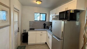 A compact kitchen with white cabinets, a stainless steel refrigerator, a microwave, and a window above the sink.