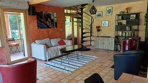Una sala de estar con sofá, mesa de comedor, un reposapiés rojo, una escalera de caracol y una estantería.