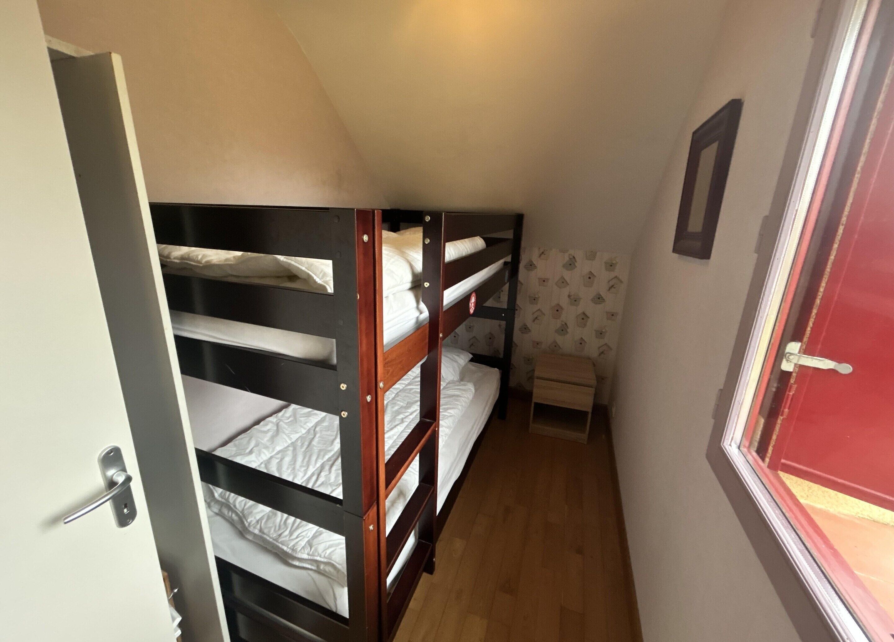 A small room with bunk beds, a wooden stool, and a window with curtains.