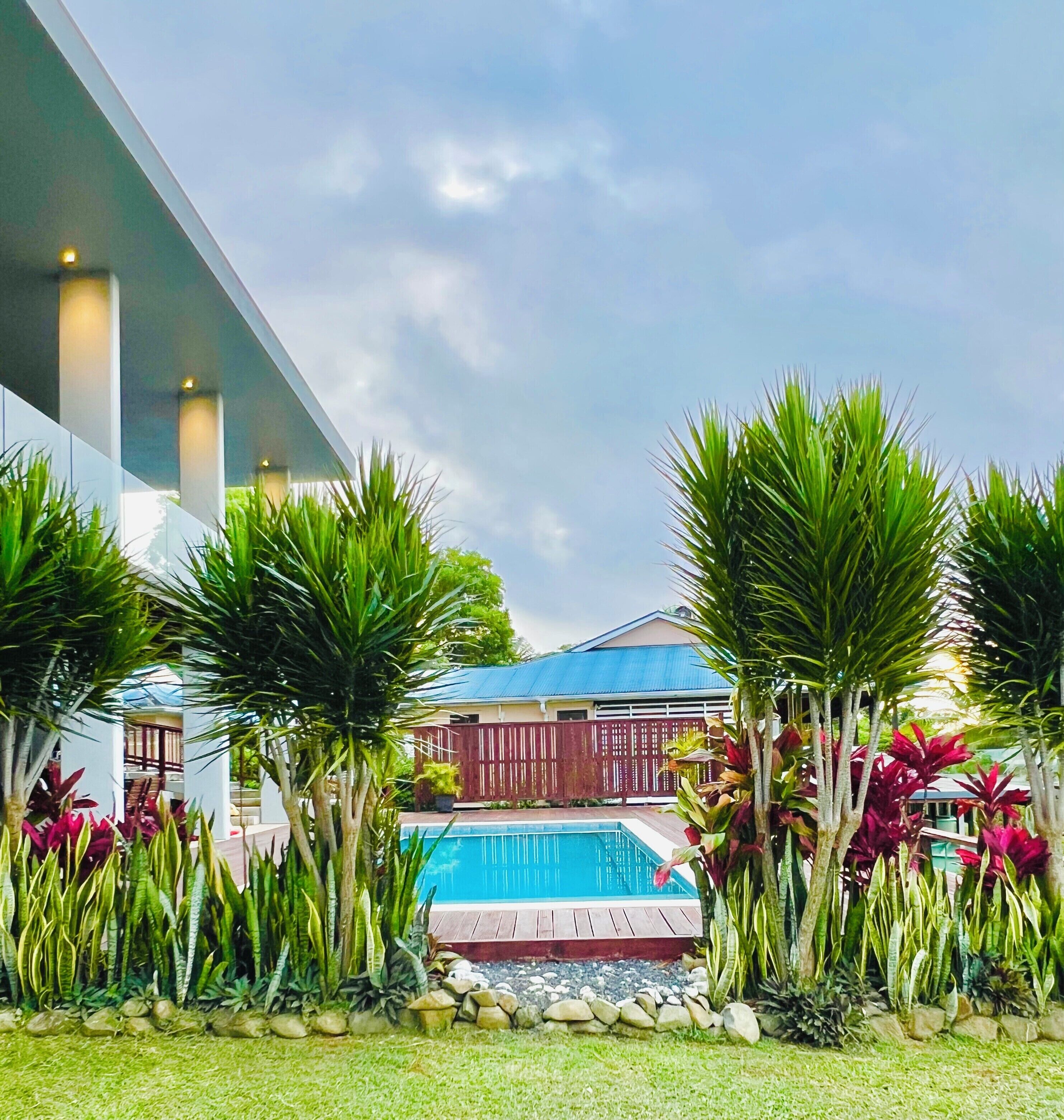 A modern building with a pool surrounded by tropical plants and a clear sky.