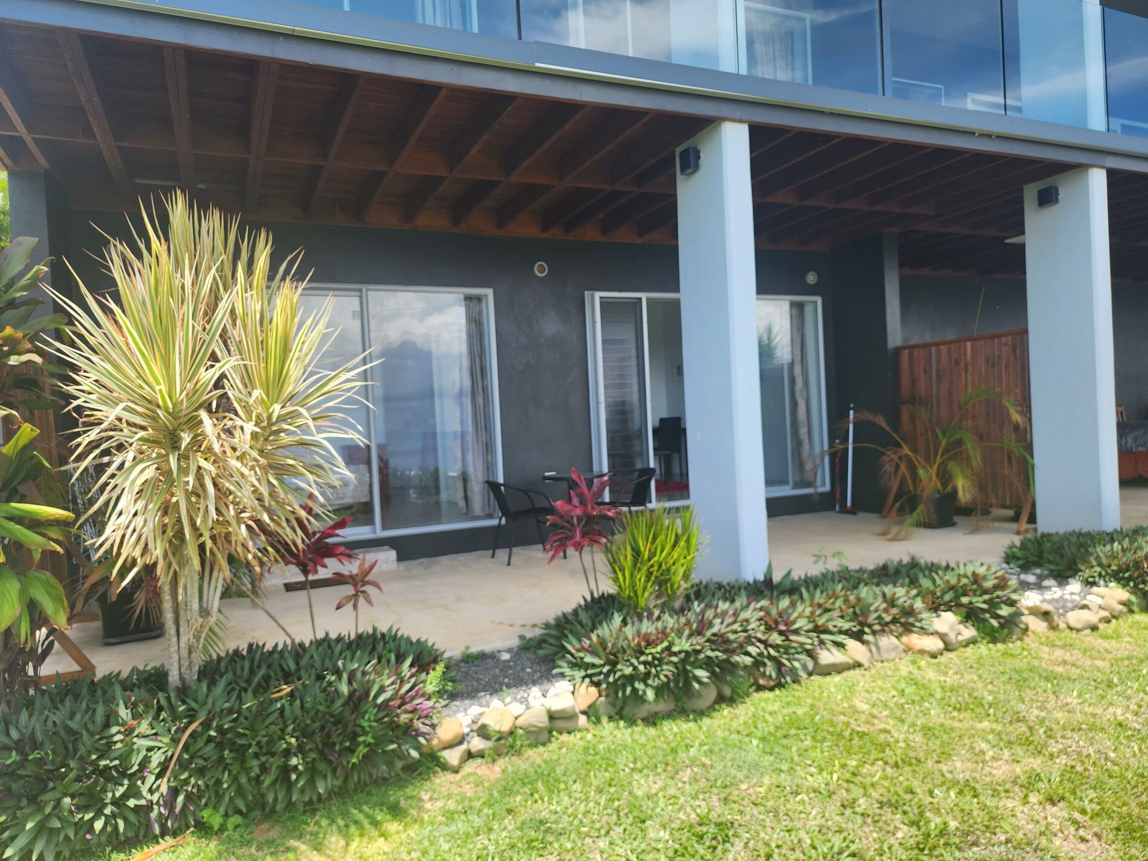 A modern building with a covered patio area, large windows, and a variety of potted plants.