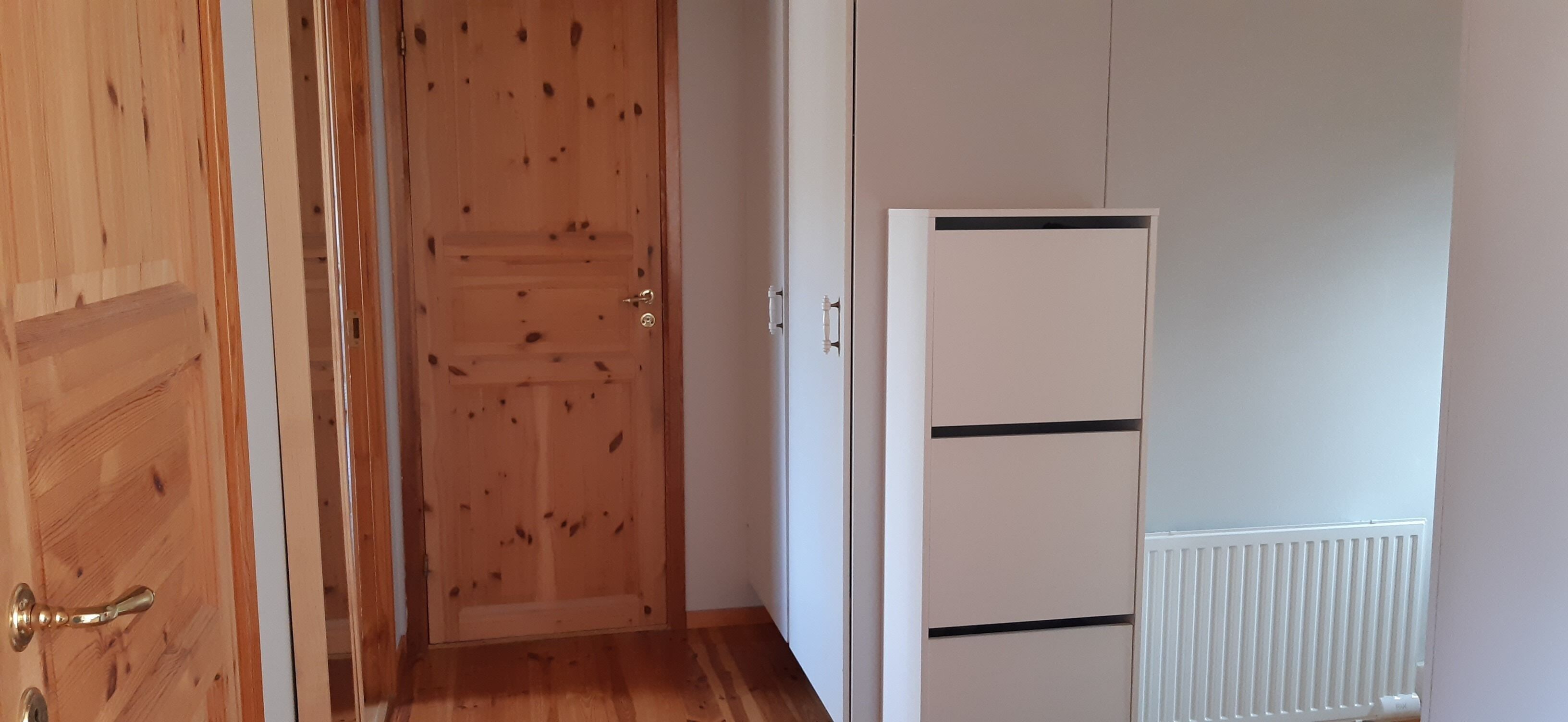 Een gang met een houten deur, een witte inbouwkast en een radiator.