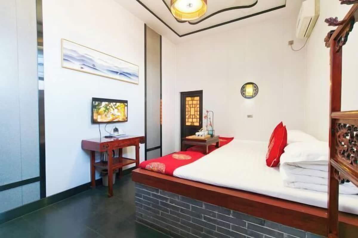 A hotel room with a bed, a desk, a television, and a wall-mounted light fixture.