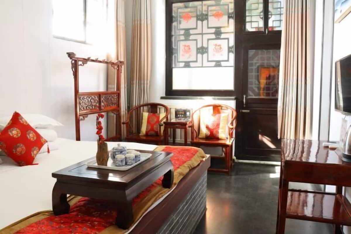 A traditional room with a bed, a wooden chair, a table with a tray, and a TV.