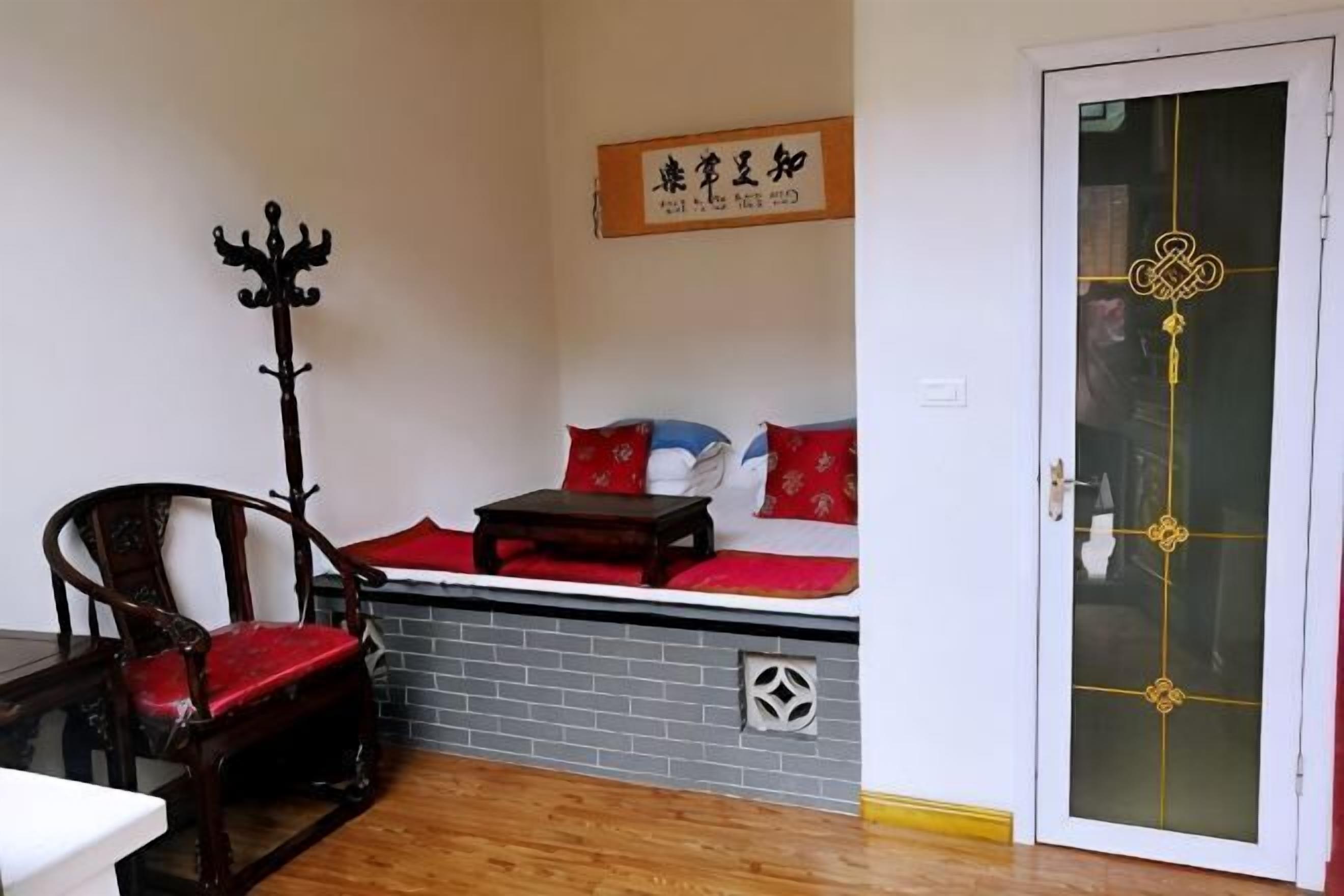 A room with a wooden floor, a sofa with red cushions, a wooden chair, a coat rack, and a door with a decorative design.