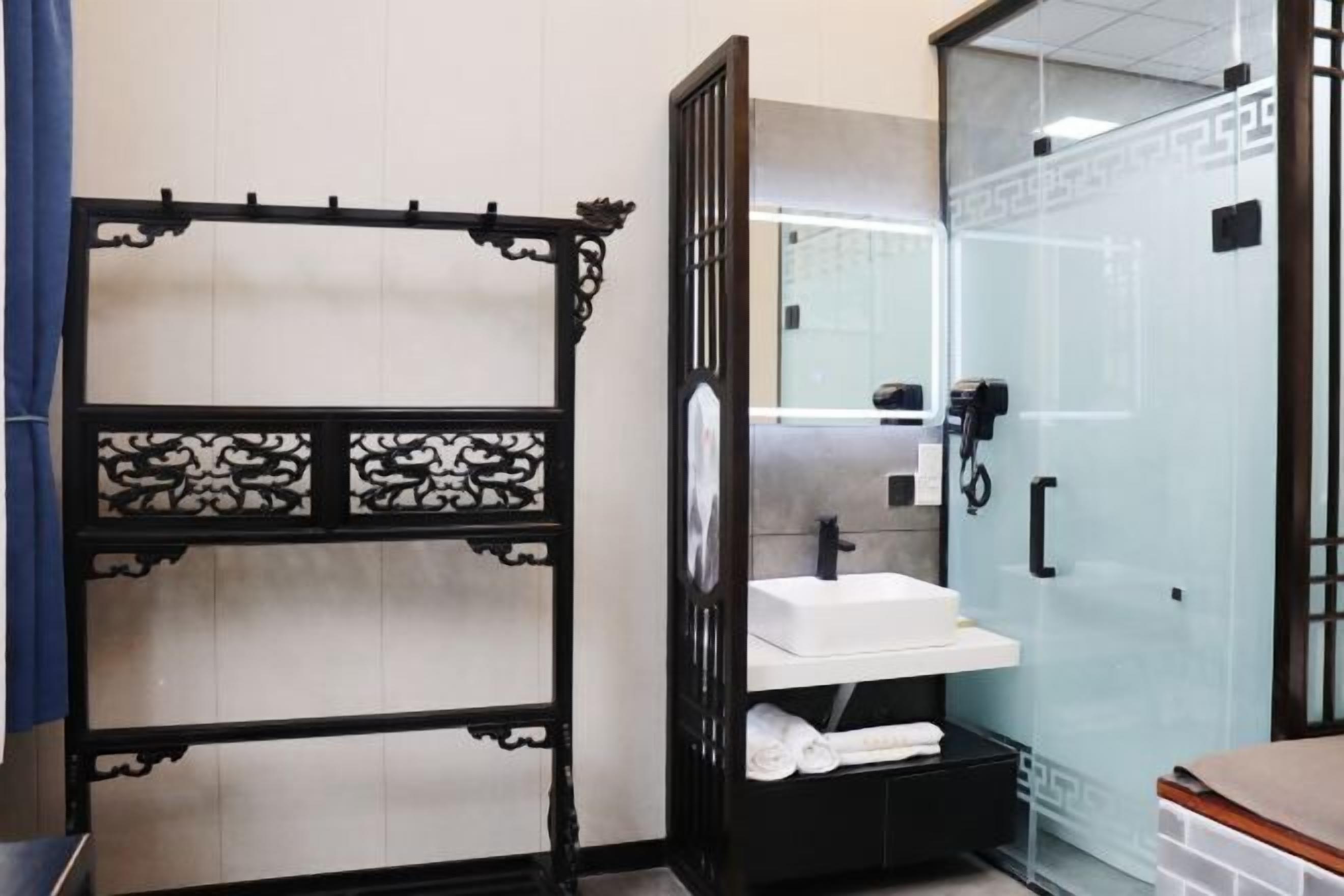 A bathroom with a glass shower enclosure, a white sink, and a black cabinet with towels.