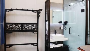 A bathroom with a glass shower enclosure, a white sink, and a black cabinet with towels.