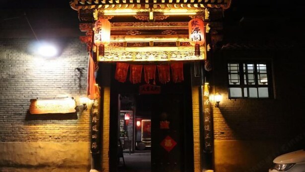 A traditional Chinese gate with intricate carvings and red lanterns, leading into a building with a brick wall and a window. - Ju Yuan Ge Inn (Pingyao Ancient City North Gate) (Pingyao County)