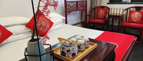A neatly arranged hotel room with a bed, a tray with teapots, a vase with flowers, and traditional chairs.