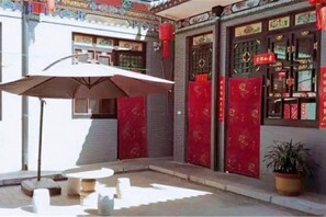 An outdoor seating area with tables and chairs, a potted plant, and a red door with a sign. - Ju Yuan Ge Inn (Pingyao Ancient City North Gate) (Pingyao County)