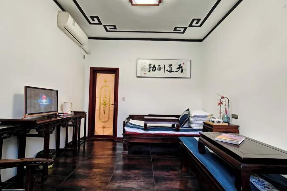 A traditional room with a wooden bed, a television on a wooden table, and a wall with calligraphy.