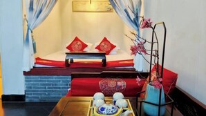 A traditional room with a bed, a wooden bench, a tea set, and a vase with flowers. - Ju Yuan Ge Inn (Pingyao Ancient City North Gate) (Pingyao County)