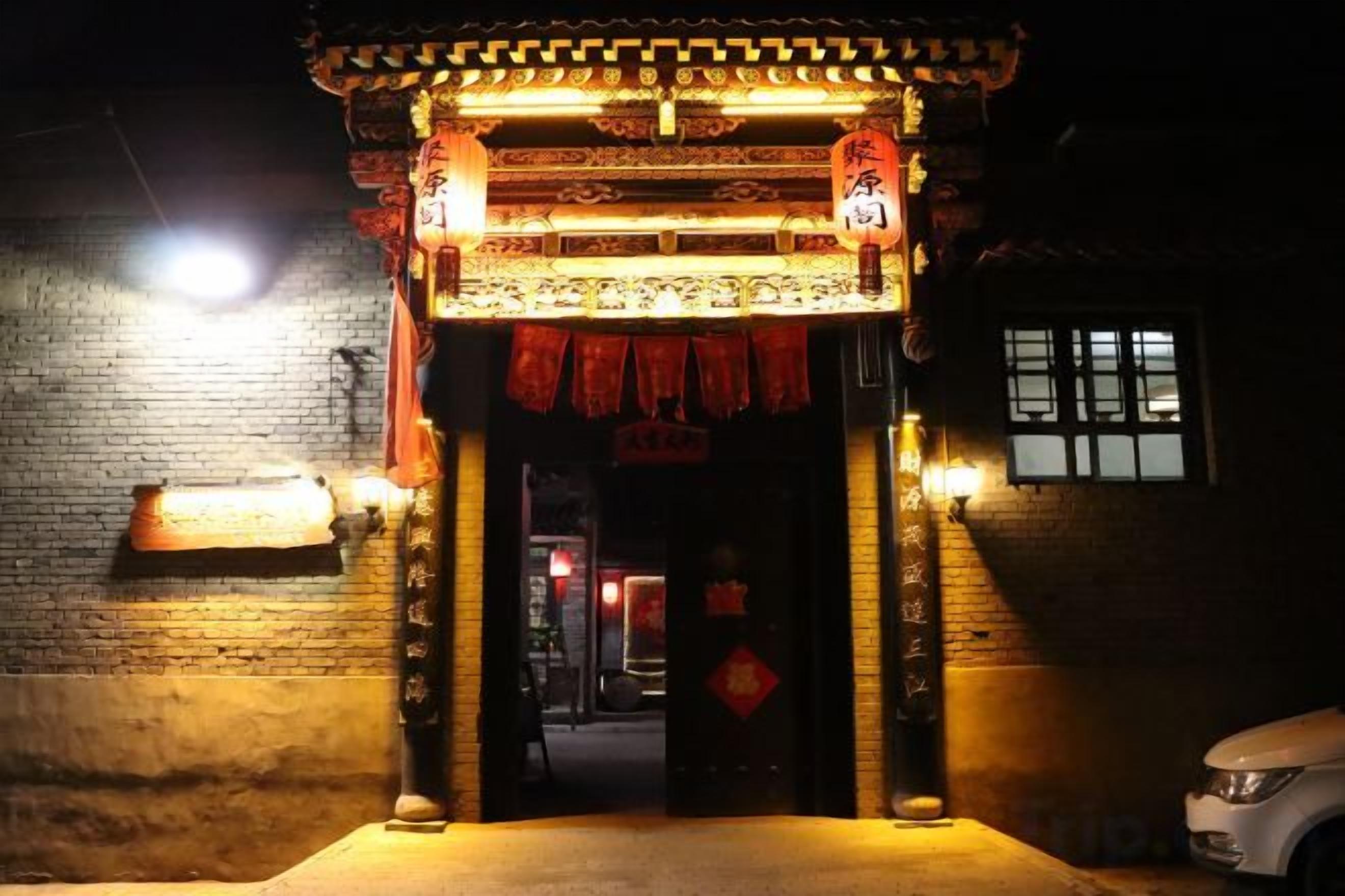 Une porte chinoise traditionnelle, ornée de motifs complexes et de décorations rouges, mène à un bâtiment dont la façade est en briques.