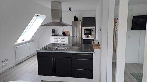 A modern kitchen with a built-in oven, a stainless steel refrigerator, and a large window providing natural light.