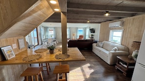 A cozy, rustic interior with a wooden dining table, chairs, a sofa, and a TV.