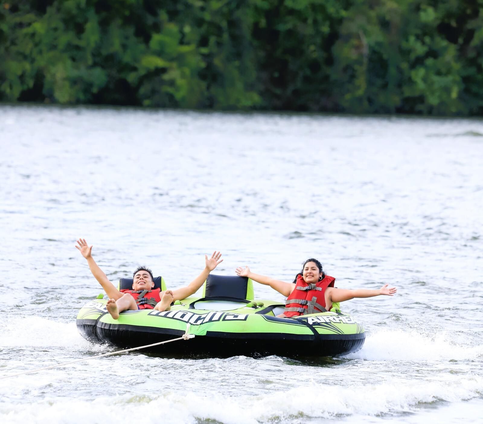 Two people on a green inflatable watercraft with the word "AIRHEAD" on it.