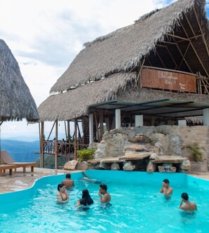 Un área de piscina con estructuras de techo de paja y un letrero que dice 'Chullahagni Wosi'.