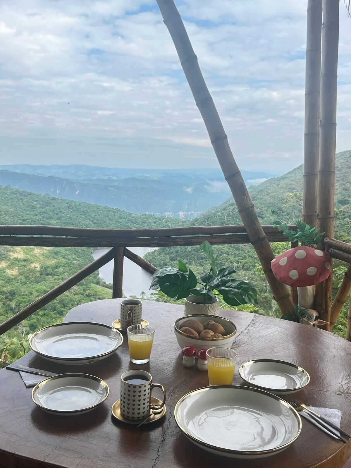 Una mesa servida con platos, tazas y un tazón de galletas, con vistas a un paisaje montañoso.
