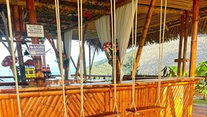 Un espace extérieur aménagé avec une structure en bambou et un toit de chaume, un panneau indiquant qu'il est interdit de faire preuve de discrimination, et une vue sur la mer.