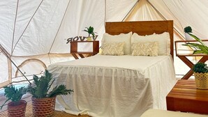 Une tente équipée d’un lit, d’oreillers, d’une tête de lit en bois et de deux plantes en pot.