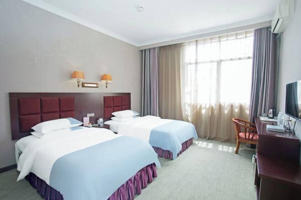 Habitación de hotel con dos camas, un escritorio, una silla y un televisor.