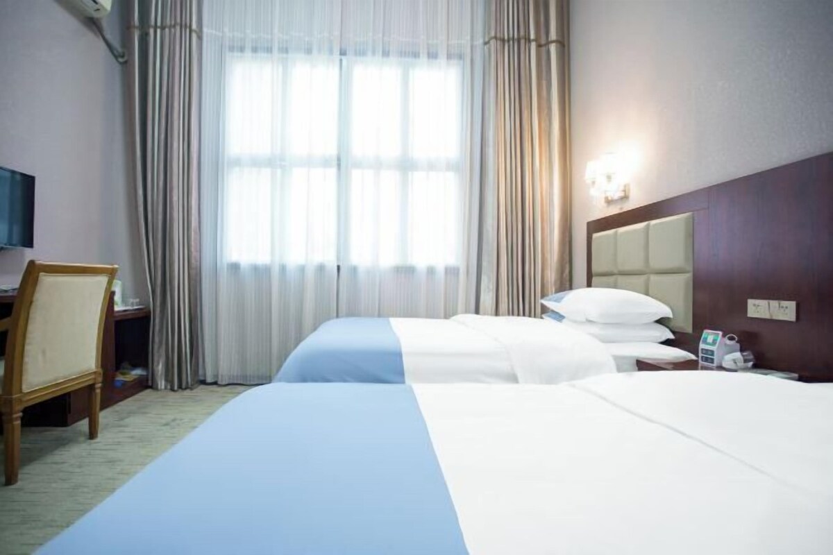 A hotel room with two beds, a desk, a chair, a TV, and a window with curtains.